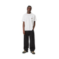 Carhartt WIP Landon Pant black tone washed combinado en look completo con camiseta blanca de bolsillo y botas de montaña, mostrando la silueta ancha y el largo del pantalón.