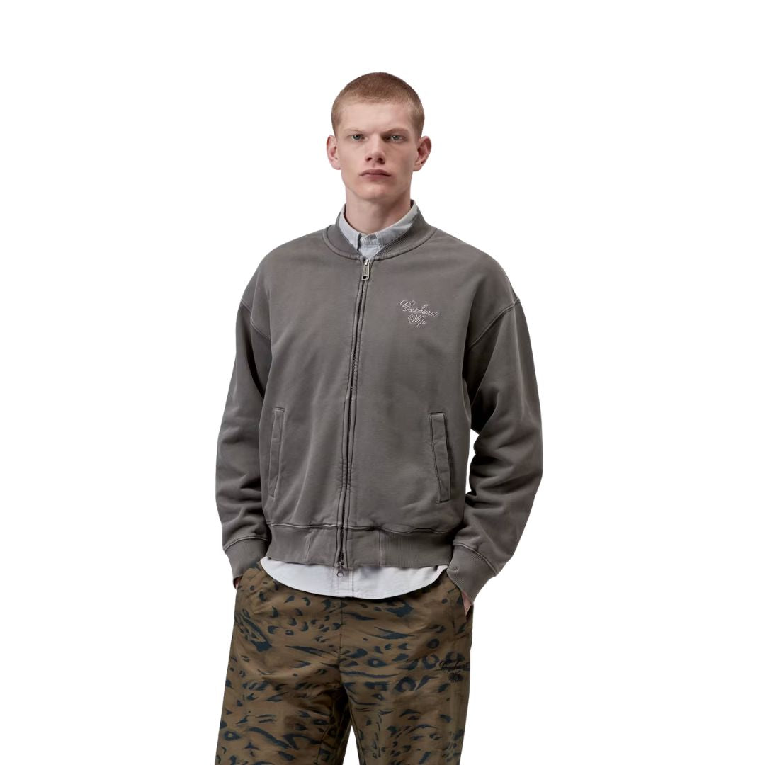 Hombre llevando chaqueta bomber Carhartt WIP gris garment dyed con cremallera frontal y bolsillos laterales.