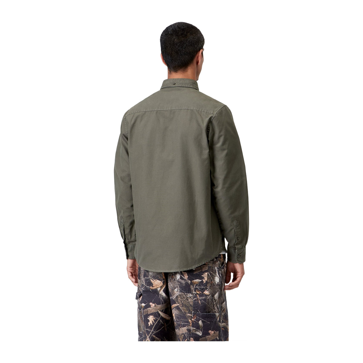 Vista trasera de modelo con la camisa Oxford de manga larga Carhartt WIP L/S Bolton Shirt en color Shungite, teñida en prenda, sobre fondo blanco liso.