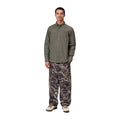 Modelo de cuerpo entero con la camisa Carhartt WIP L/S Bolton Shirt en color Shungite, combinada con pantalón estampado de camuflaje y zapatillas claras.