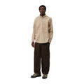 Modelo de cuerpo entero con la camisa de pana Carhartt WIP L/S Madison Cord Shirt en color Wall, combinada con pantalón cargo marrón oscuro y zapatillas.