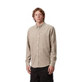 Modelo en plano medio con la camisa de pana Carhartt Madison beige abrochada, cuello abotonado, puños de manga larga y pequeño logo bordado en el pecho, con pantalón negro.