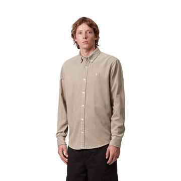 Modelo en plano medio con la camisa de pana Carhartt Madison beige abrochada, cuello abotonado, puños de manga larga y pequeño logo bordado en el pecho, con pantalón negro.