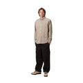 Modelo con la camisa de pana Carhartt Madison beige, manga larga y cuello abotonado, combinada con pantalón cargo negro y botas de montaña, de pie con las manos en los bolsillos.
