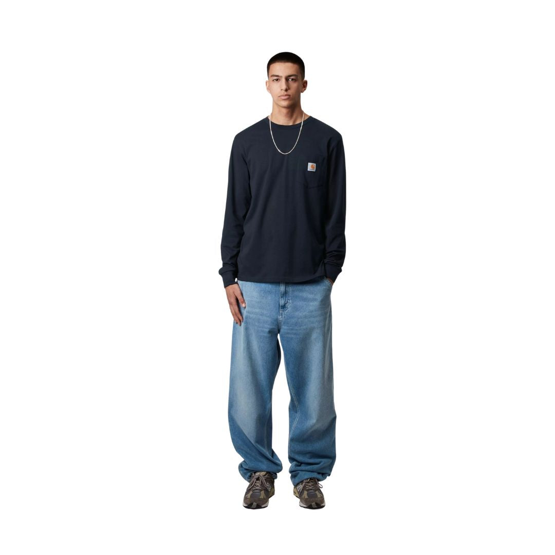 Modelo con camiseta carhartt wip l/s pocket t-shirt azul marino oscuro combinada con pantalón vaquero ancho.