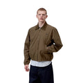 Carhartt WIP Madison Ripstop Jacket Dark Beech, modelo masculino de tres cuartos con mano en bolsillo, detalle del puño elástico y textura ripstop del tejido teñido en prenda.