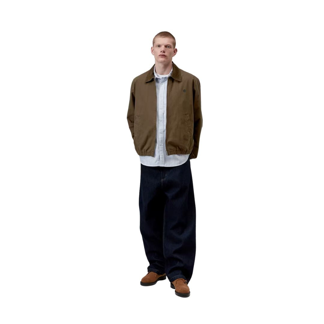 Carhartt WIP Madison Ripstop Jacket Dark Beech, modelo masculino de cuerpo entero de frente con corte relajado, camisa de rayas asomando bajo el bajo elástico.