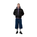 Carhartt WIP Madison Ripstop Jacket negro wax, modelo masculino de frente con cremallera cerrada y capucha lila visible, detalle del bajo elástico y bolsillo lateral
