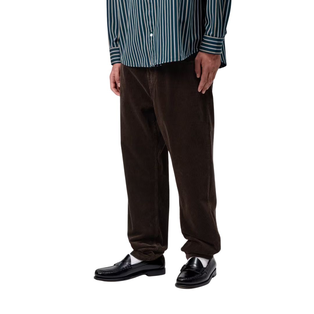 Primer plano de la parte inferior del modelo con el pantalón de pana Carhartt WIP Newel Cord Pant color marrón tobacco y mocasines negros.