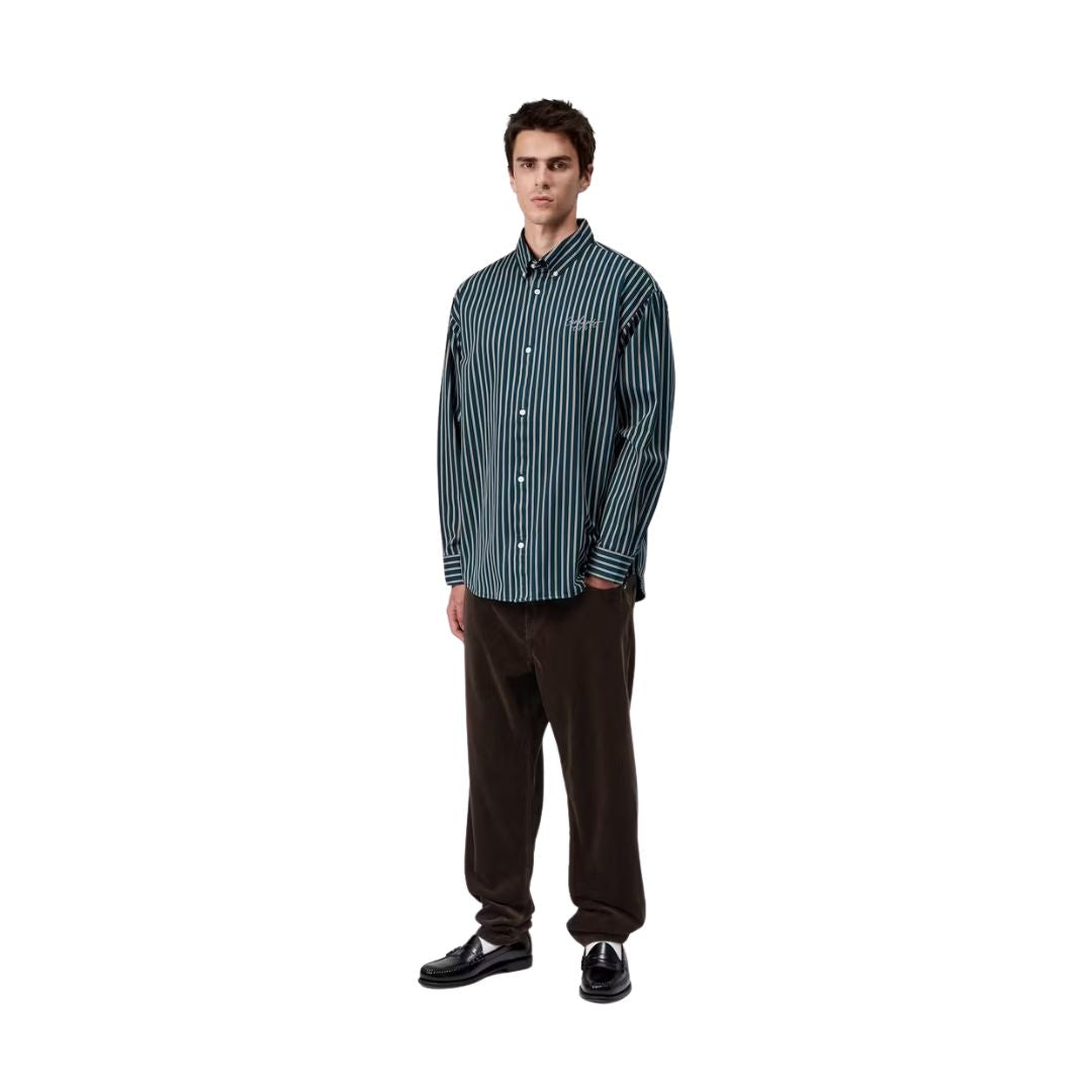 Modelo masculino vistiendo el pantalón de pana Carhartt WIP Newel Cord Pant color marrón tobacco con camisa a rayas azul.