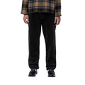 Plano frontal recortado de un modelo con el pantalón de pana Carhartt WIP Newel Pant en color negro, camisa de cuadros y mocasines, resaltando la caída recta del canalé de la pana.
