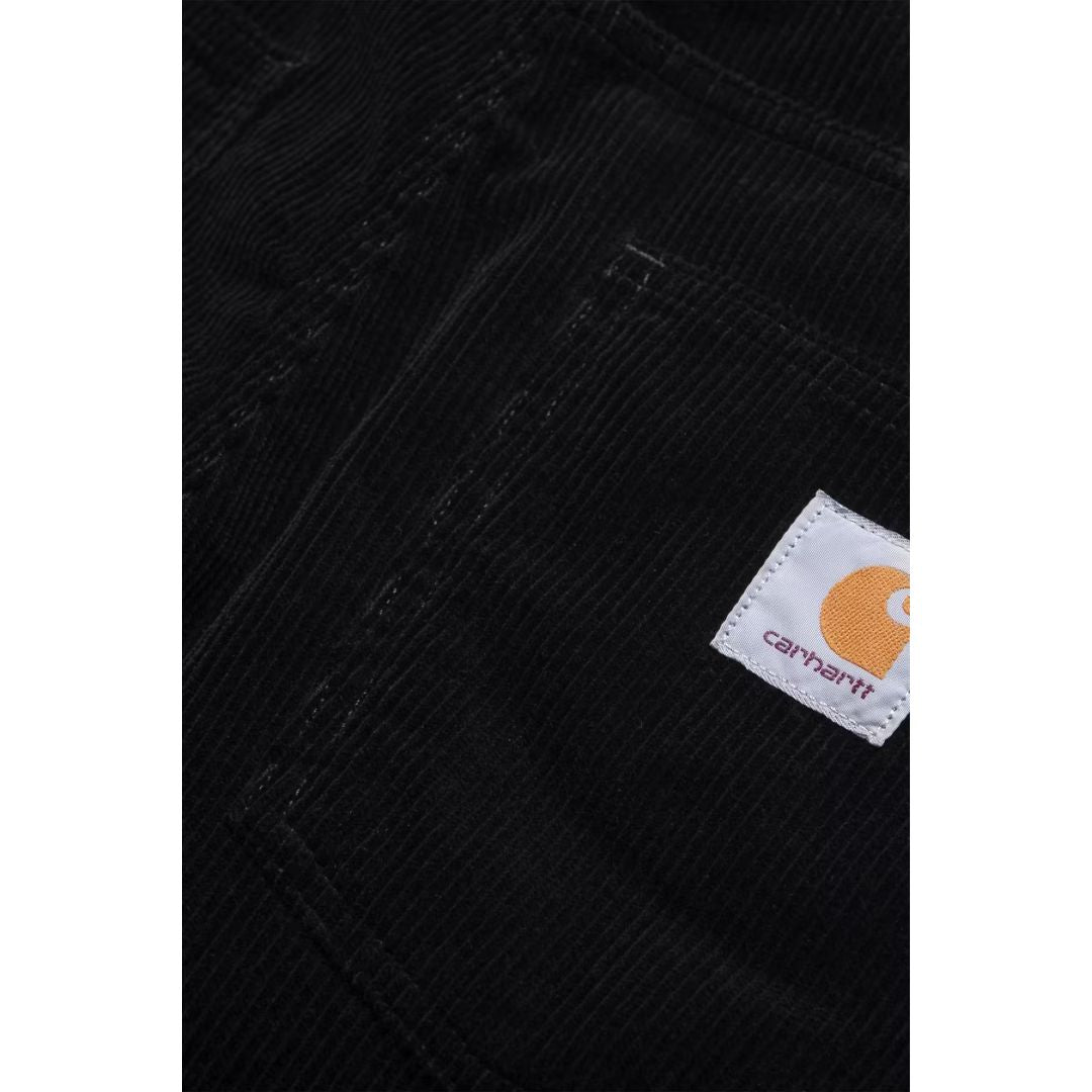 Detalle del bolsillo trasero derecho del pantalón de pana Carhartt WIP Newel Pant en color negro, con la etiqueta Square Label tejida y el canalé ancho de la pana Coventry en primer plano.