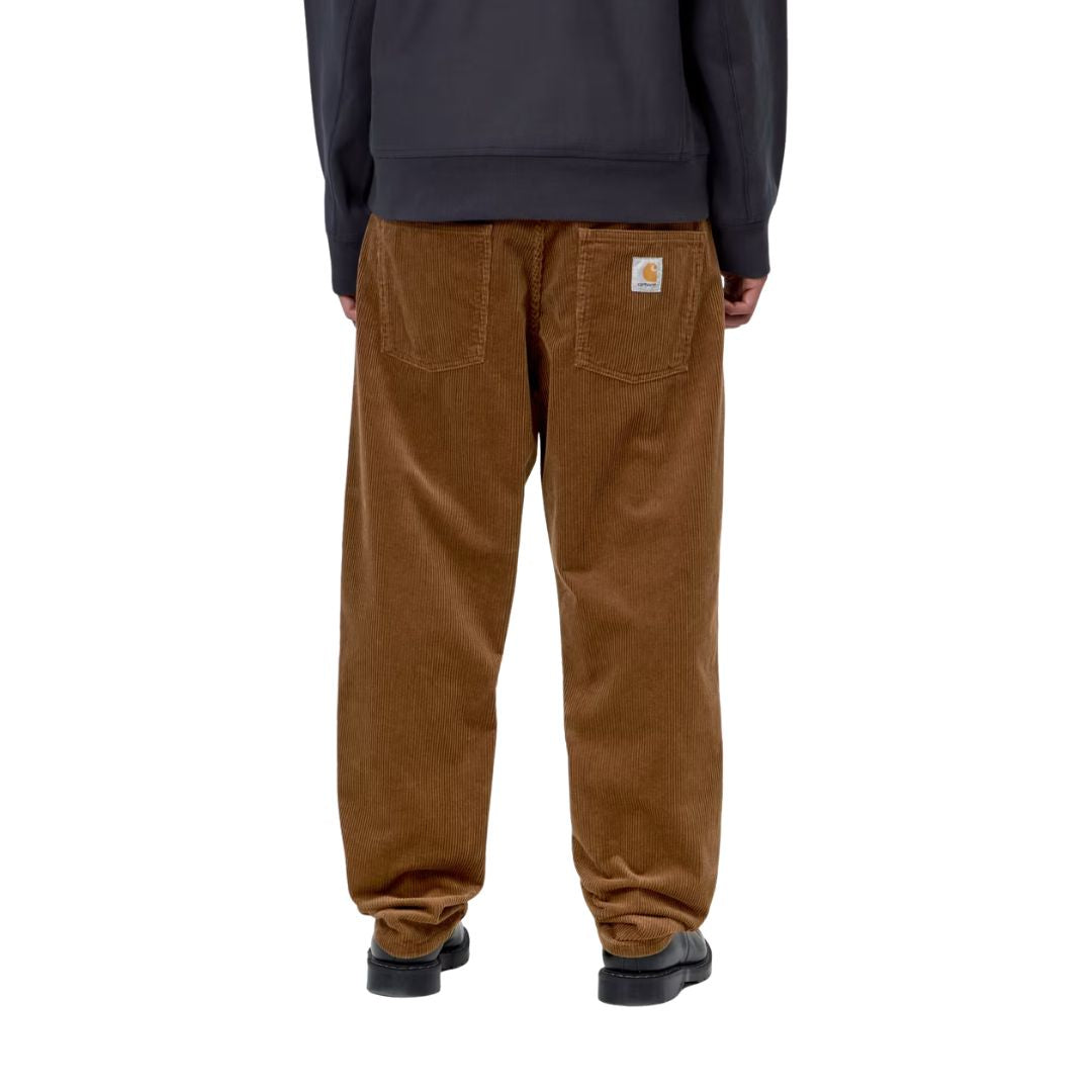 Vista trasera de un modelo con el pantalón de pana Carhartt WIP Newel Pant en color marrón cámel, mostrando los bolsillos traseros y la etiqueta Square Label tejida.