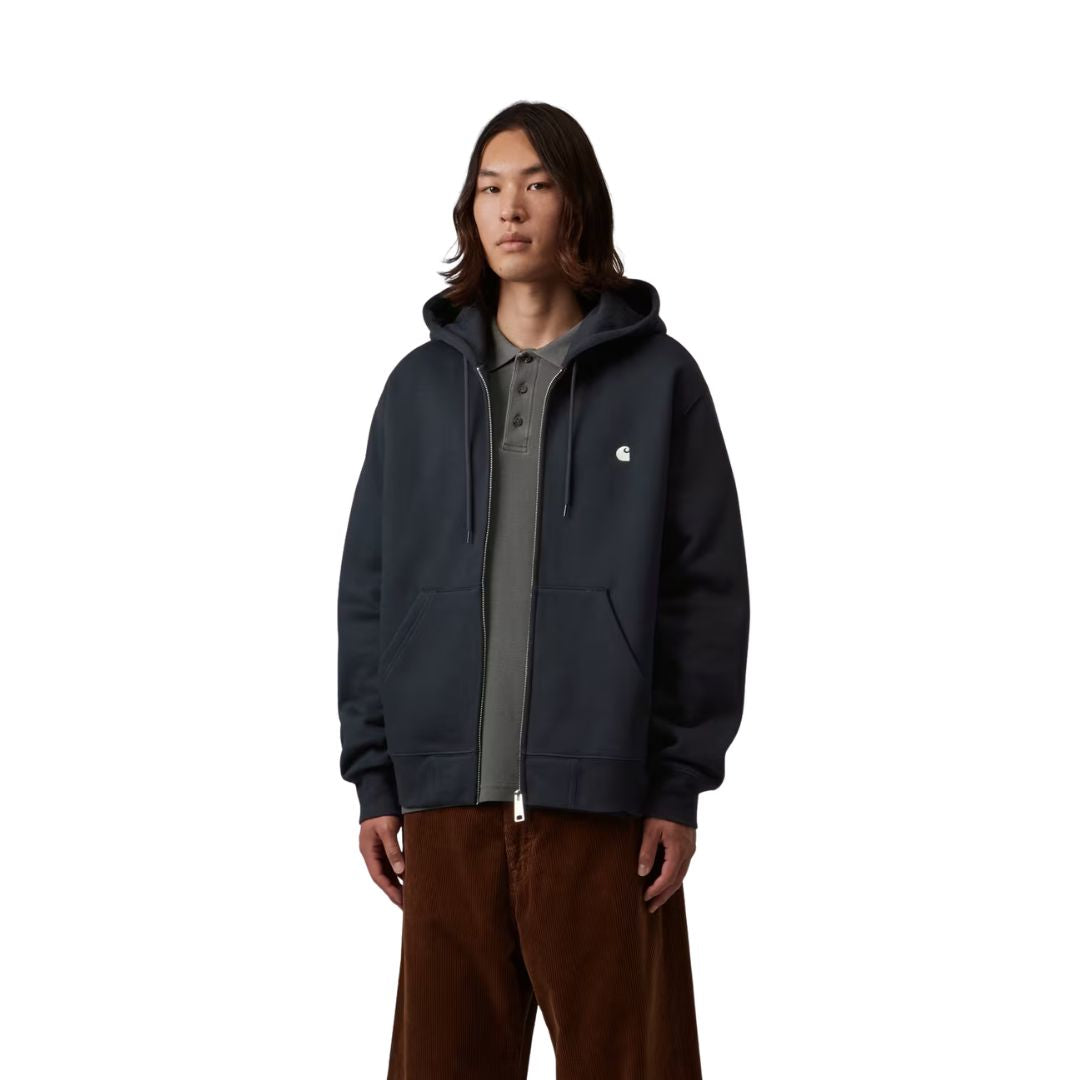 Modelo con la Carhartt WIP Hooded Mack Sweat Jacket en color dark navy wax con la cremallera abierta sobre un polo, cordones de capucha colgando y logo C bordado en el pecho, plano frontal.