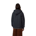 Vista trasera del modelo con la sudadera Carhartt WIP Hooded Mack Sweat Jacket en color dark navy wax, con capucha caída, hombros caídos y cintura acanalada sobre la camiseta interior.