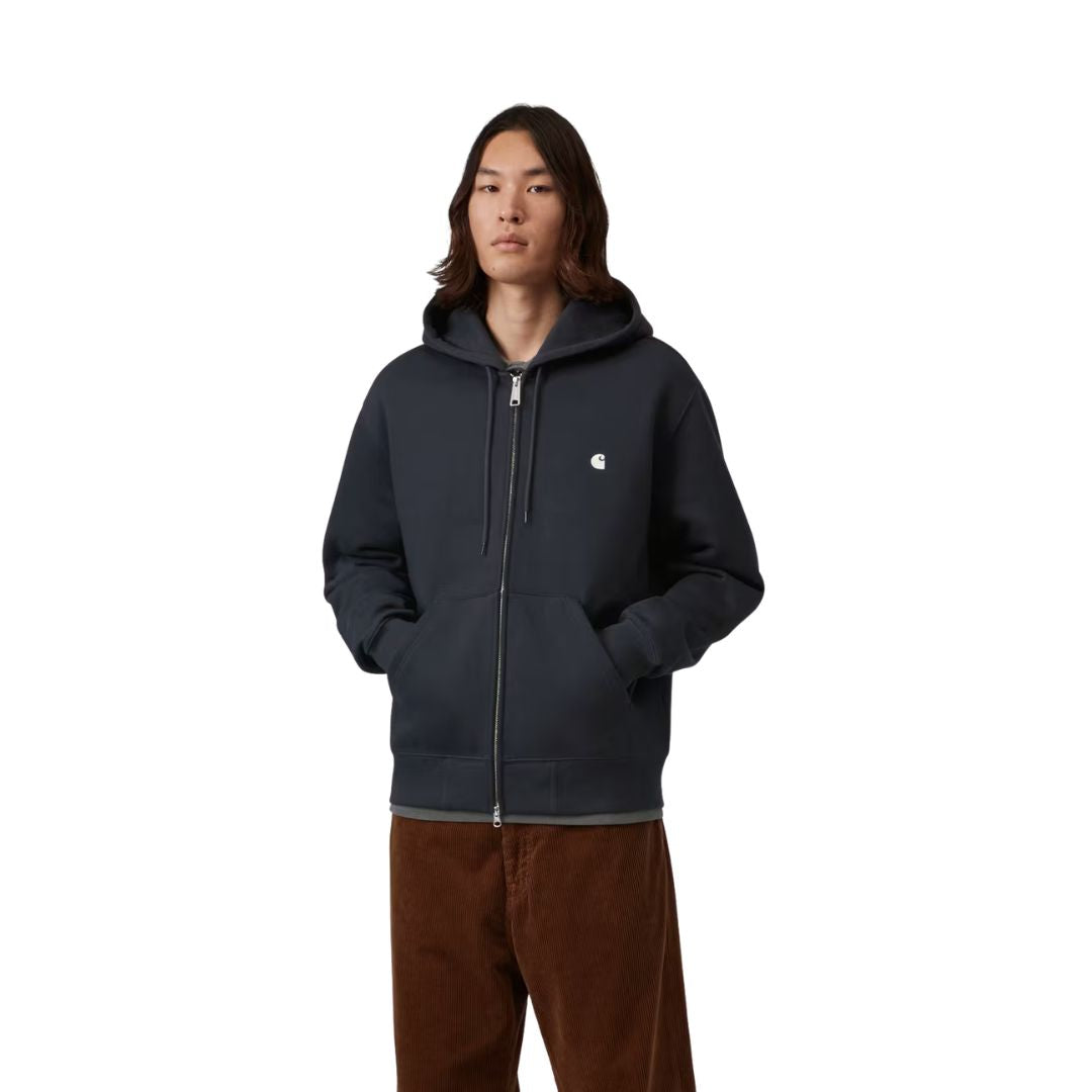 Plano medio de la Carhartt WIP Hooded Mack Sweat Jacket en color dark navy wax cerrada, con el modelo con las manos en los bolsillos canguro y el logo C bordado sobre el pecho.