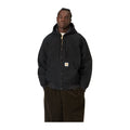 Modelo con las manos en los bolsillos y la chaqueta Carhartt WIP OG Active Jacket en color Black, con capucha, cordón de ajuste y silueta tipo bomber.