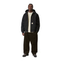 Modelo de cuerpo entero con la chaqueta con capucha Carhartt WIP OG Active Jacket en color Black, combinada con pantalón marrón oscuro de pana y botas.