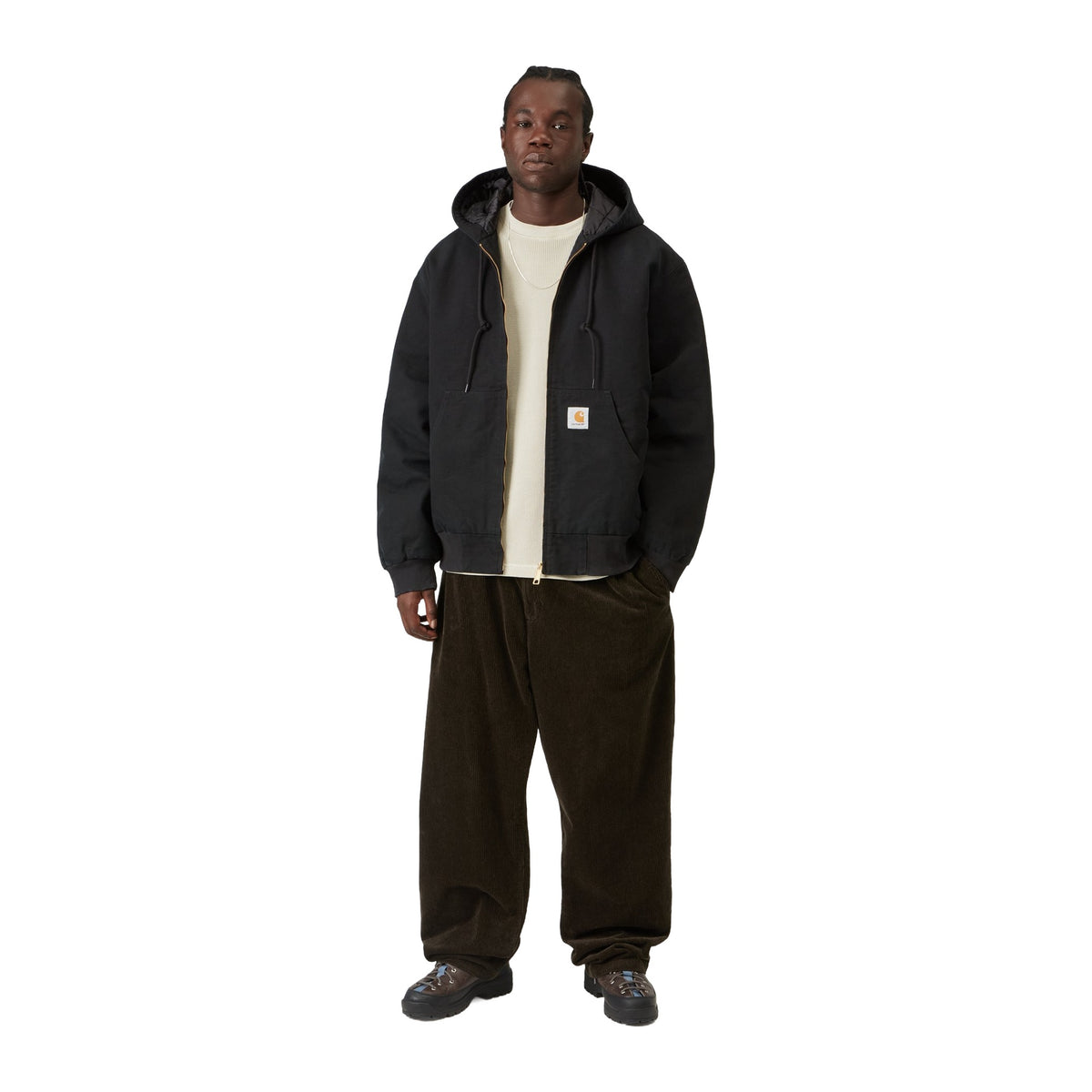 Modelo de cuerpo entero con la chaqueta con capucha Carhartt WIP OG Active Jacket en color Black, combinada con pantalón marrón oscuro de pana y botas.
