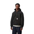 Modelo vistiendo la chaqueta Carhartt WIP OG Active Jacket negra de frente con capucha y cremallera cerrada.