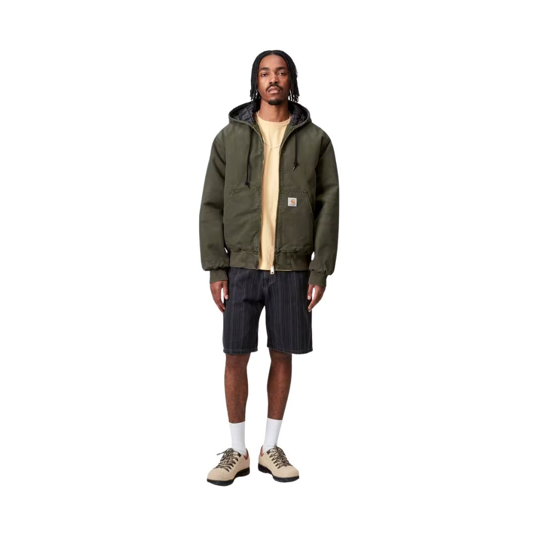 Chaqueta Carhartt WIP OG Active Jacket color oliva vista frontal con capucha y cremallera cerrada y vaqueros cortos.