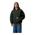 Modelo con las manos en los bolsillos y la chaqueta Carhartt WIP OG Active Jacket en color Raven, con capucha, etiqueta cuadrada y corte holgado tipo bomber.