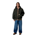 Modelo de cuerpo entero con la chaqueta con capucha Carhartt WIP OG Active Jacket en color Raven, combinada con vaqueros anchos azules y botas marrones.