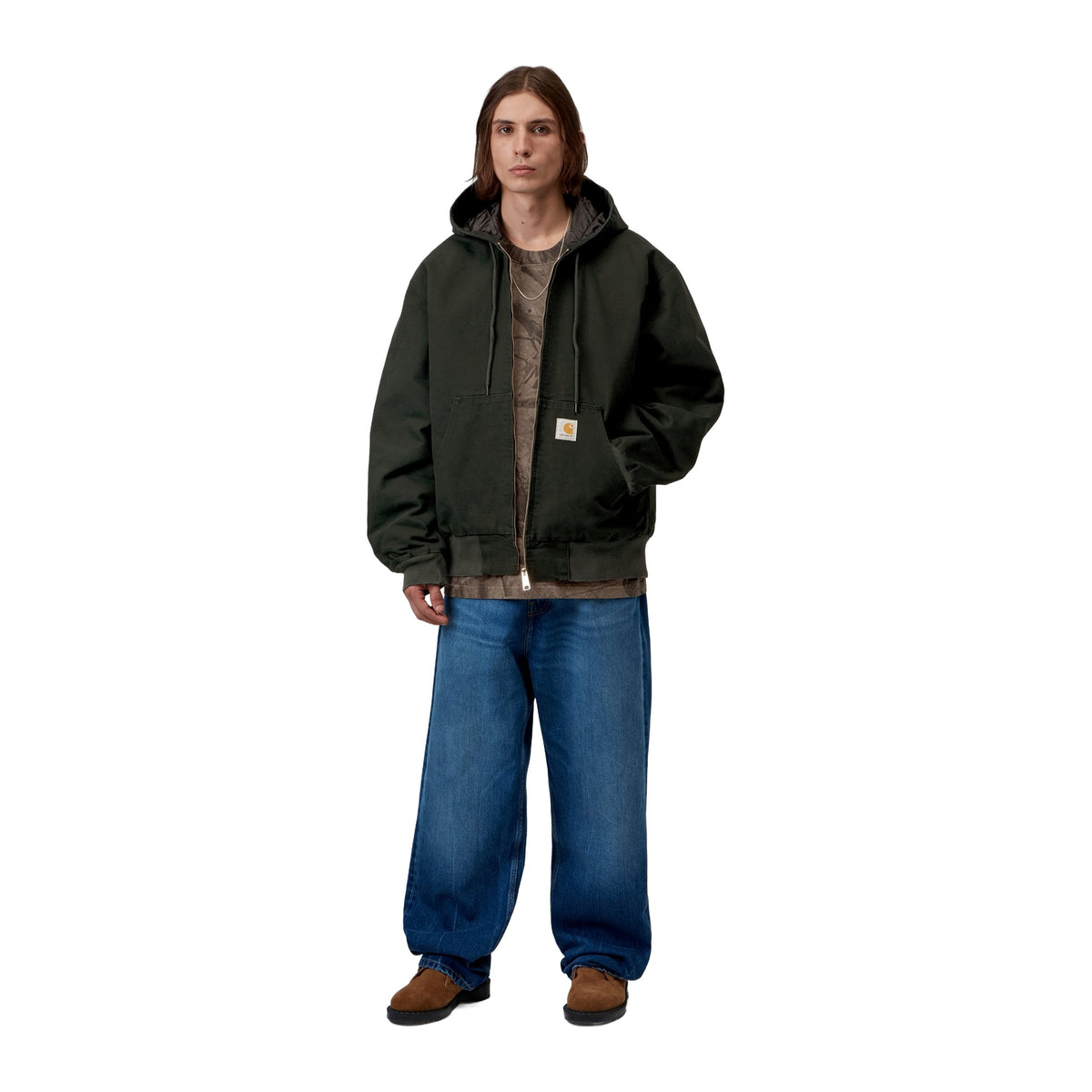 Modelo de cuerpo entero con la chaqueta con capucha Carhartt WIP OG Active Jacket en color Raven, combinada con vaqueros anchos azules y botas marrones.