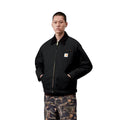 Plano medio de la Carhartt WIP OG Detroit Jacket Winter en color negro cerrada, con el modelo mostrando el cuello de pana, la cremallera dorada y la etiqueta Carhartt WIP en el pecho.