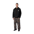 Modelo con la Carhartt WIP OG Detroit Jacket Winter en color negro abierta sobre un jersey, con pantalón estampado, mostrando de cuerpo entero el corte holgado y el cuello de pana.