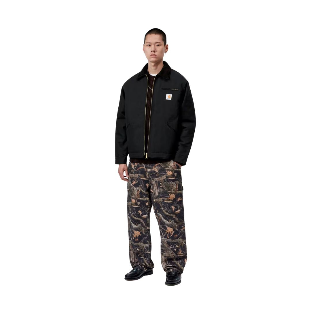 Modelo con la Carhartt WIP OG Detroit Jacket Winter en color negro abierta sobre un jersey, con pantalón estampado, mostrando de cuerpo entero el corte holgado y el cuello de pana.