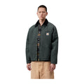 Modelo de frente con la chaqueta acolchada Carhartt WIP OG Detroit Jacket en color Raven / Black, con cuello oscuro, cremallera y etiqueta cuadrada en el pecho.