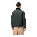 Vista trasera de modelo con la chaqueta acolchada Carhartt WIP OG Detroit Jacket en color Raven / Black, con cuello oscuro y bajo recto, sobre fondo blanco liso.