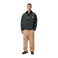 Modelo de cuerpo entero con la chaqueta acolchada Carhartt WIP OG Detroit Jacket en color Raven / Black, combinada con pantalón beige y zapatos negros.