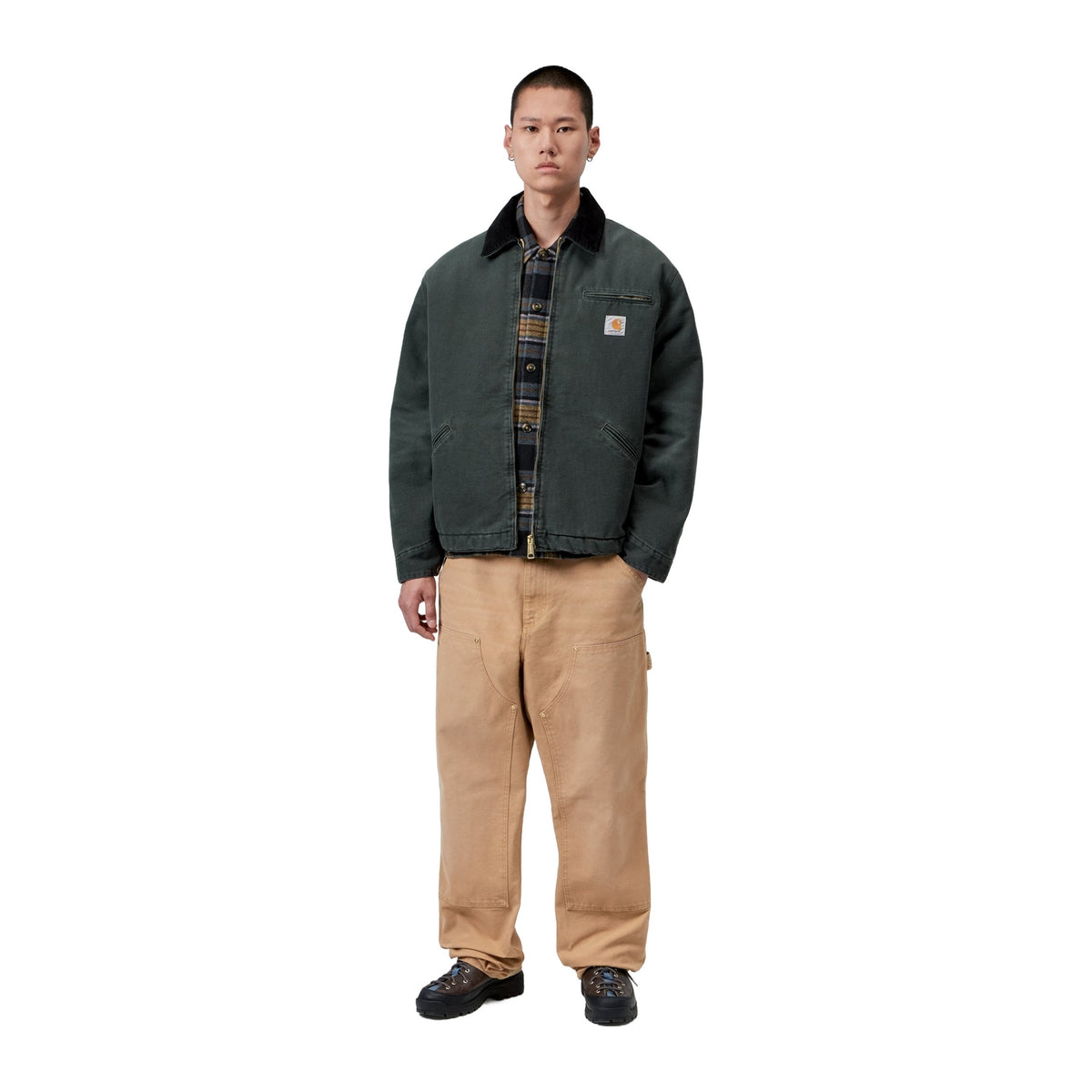 Modelo de cuerpo entero con la chaqueta acolchada Carhartt WIP OG Detroit Jacket en color Raven / Black, combinada con pantalón beige y zapatos negros.