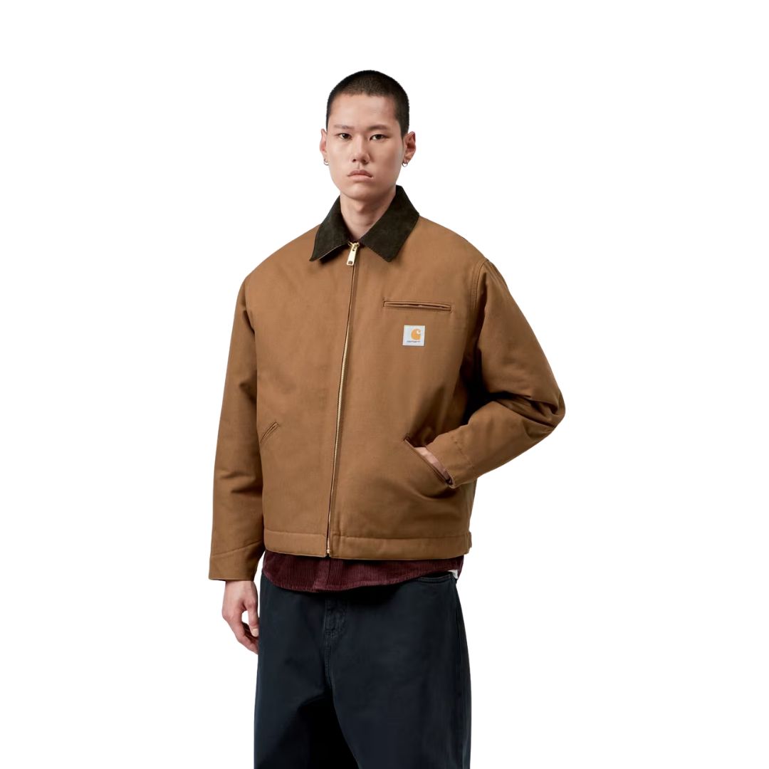 Plano medio de la Carhartt WIP OG Detroit Jacket Winter en color marrón cerrada, con el modelo mostrando el cuello de pana oscuro, la cremallera dorada y la etiqueta Carhartt WIP.
