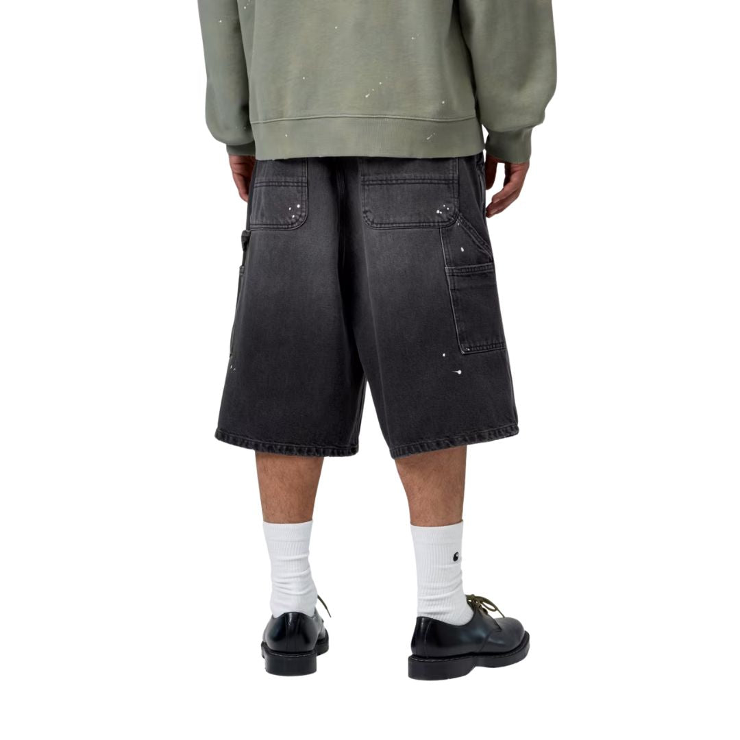 Carhartt WIP OG Single Knee Short negro destroy wash, vista trasera en modelo, bolsillos workwear grandes con toques de pintura blanca y Square Label tejida.