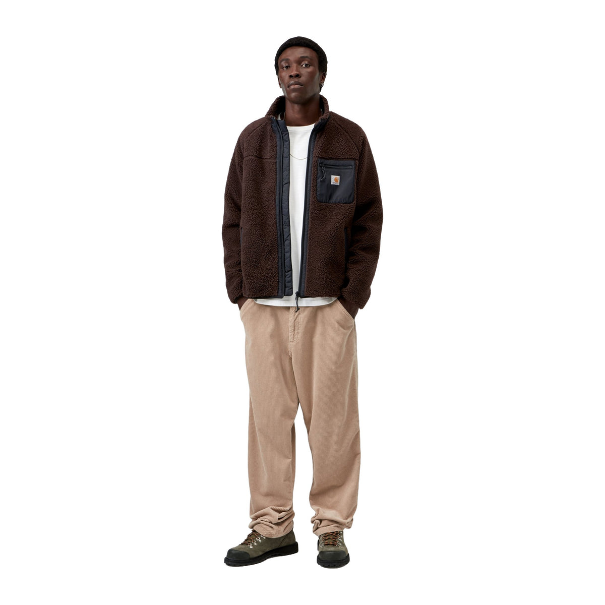Modelo de cuerpo entero con la chaqueta forro polar Carhartt WIP Prentis Liner en color Palisander / Black, combinada con pantalón beige ancho y zapatillas.