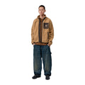 Modelo de cuerpo entero con la chaqueta forro polar Carhartt WIP Prentis Liner en color WIP Dusty H / Tobacco, con vaqueros anchos desgastados y zapatillas.