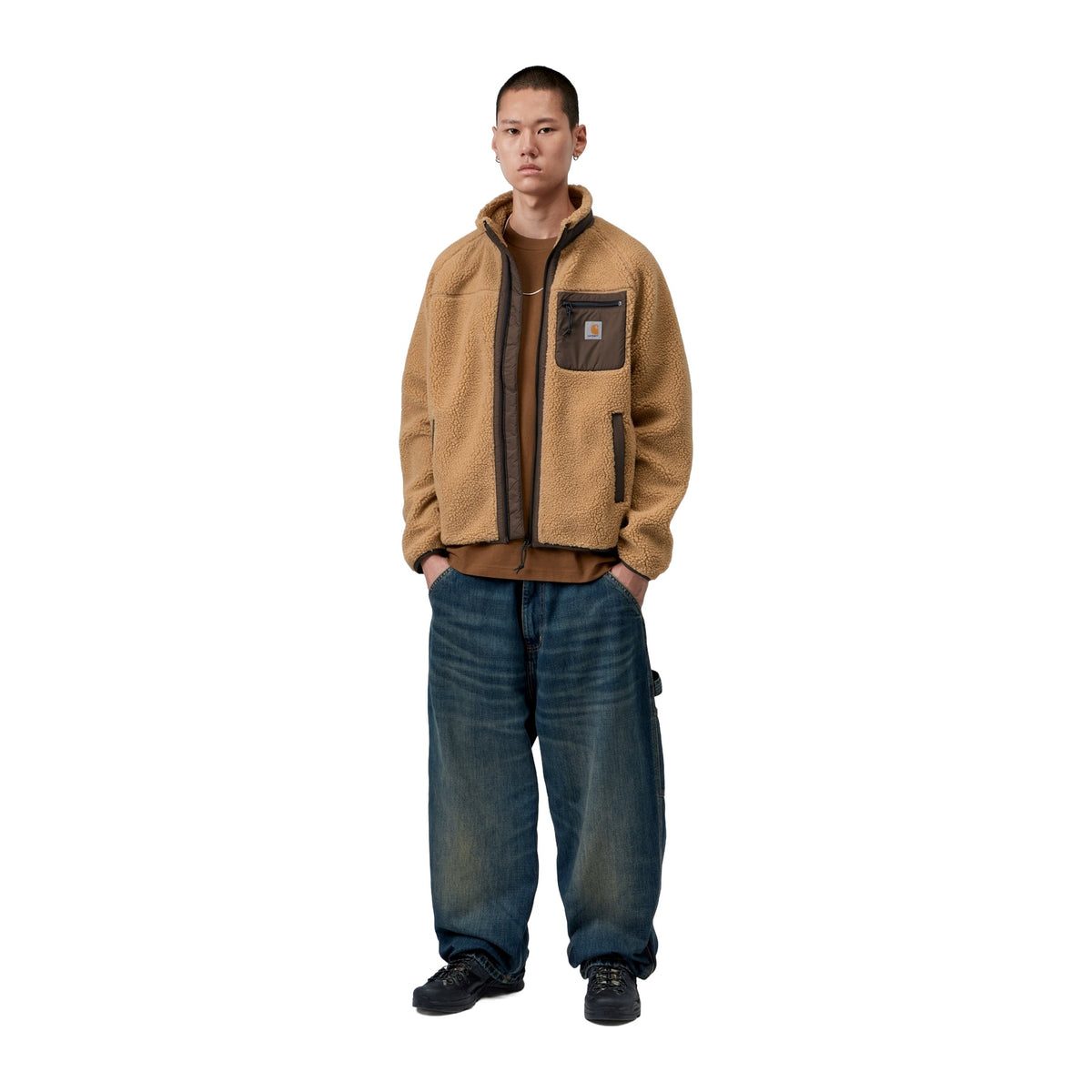 Modelo de cuerpo entero con la chaqueta forro polar Carhartt WIP Prentis Liner en color WIP Dusty H / Tobacco, con vaqueros anchos desgastados y zapatillas.