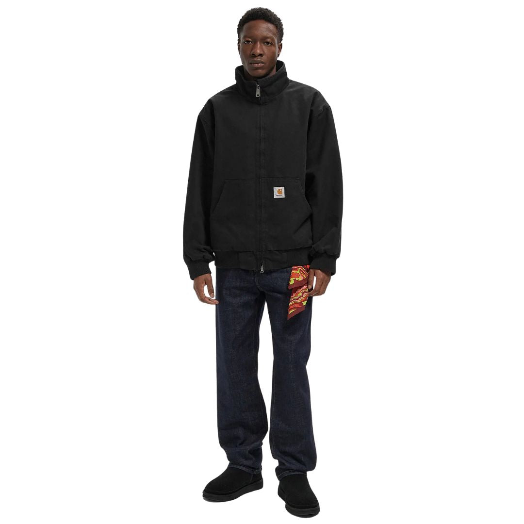 Modelo vistiendo la chaqueta Carhartt WIP Ravon Jacket en color Black Heavy Stone Wash, cierre con cremallera y cuello alto.