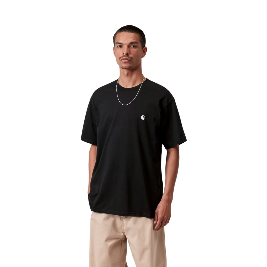 Carhartt WIP S/S Madison T-Shirt black/white en plano frontal sobre modelo, con pantalón beige ancho, resaltando el logotipo bordado en blanco sobre el pecho negro.