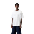 Carhartt WIP S/S Madison T-Shirt white/black en plano frontal sobre modelo, con pantalón vaquero ancho, resaltando el cuello redondo y el logotipo bordado en el pecho.