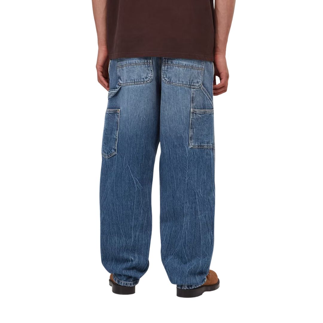 Vista trasera en modelo del pantalón Carhartt WIP Single Knee Pant en Blue Stone Washed, con bolsillos traseros reforzados y bolsillo de rodilla lateral visible.