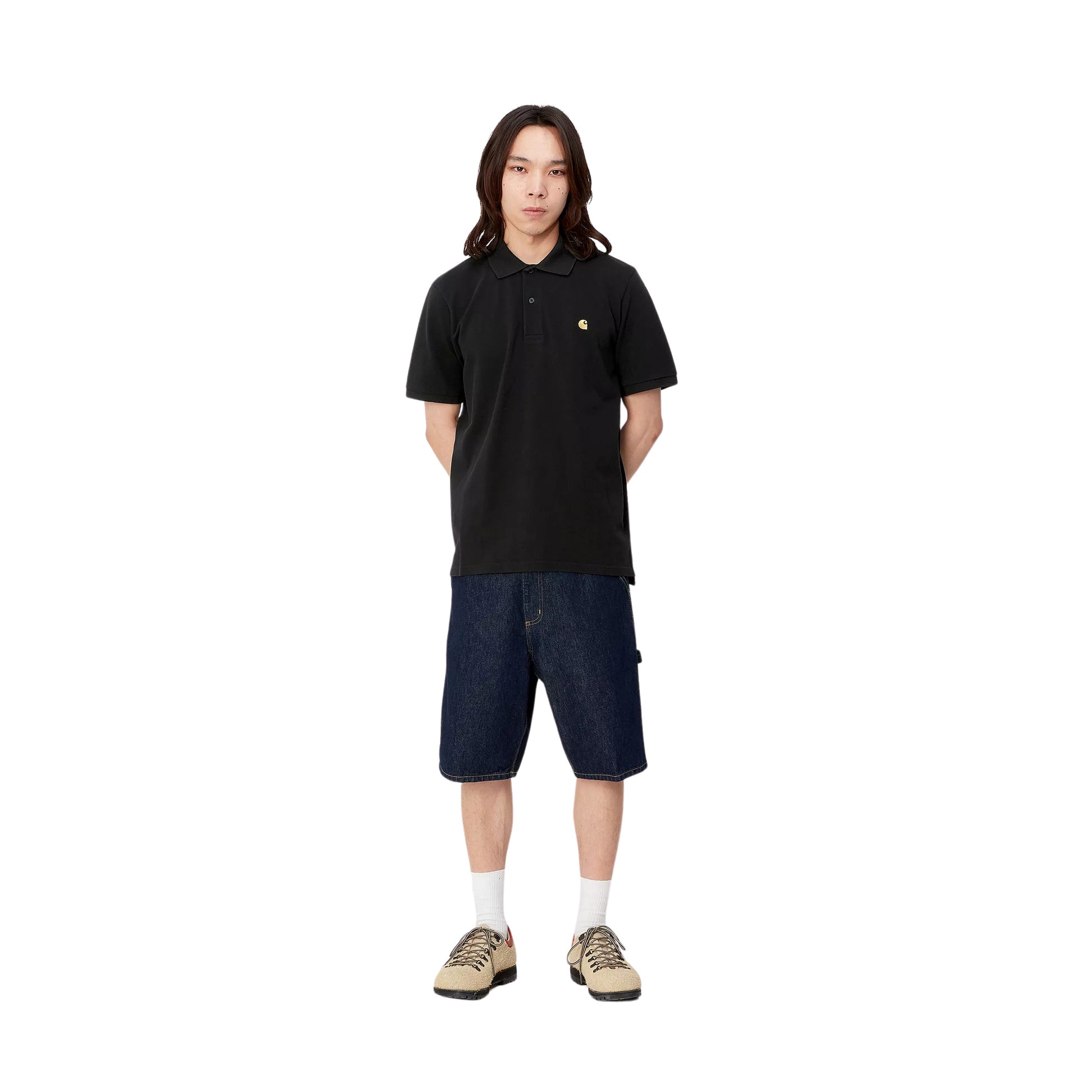 Modelo con el polo Carhartt WIP S/S Chase Pique negro con el logo bordado en dorado y shorts vaqueros