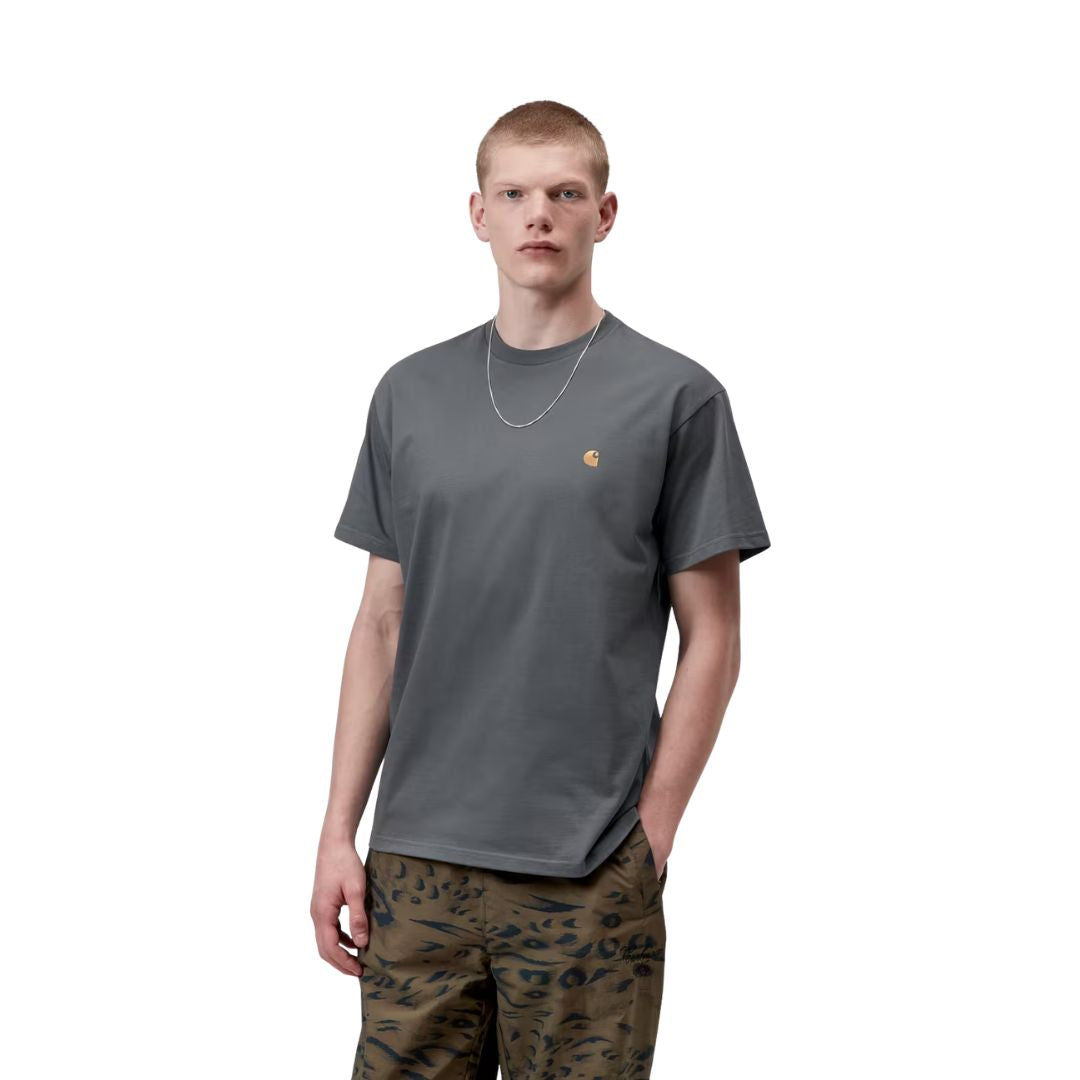 Carhartt WIP S/S Chase T-Shirt en color styx con detalle dorado, vista frontal sobre modelo masculino. Camiseta de algodón de manga corta en gris pizarra oscuro con cuello redondo y logotipo "C" de Carhartt WIP bordado en dorado en el pecho izquierdo. Corte loose fit. Combinada con pantalón de estampado animal print caqui y cadena plateada.