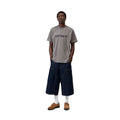 Modelo con camiseta Carhartt WIP S/S Script T-Shirt en Shady Grey y logo Script en Dark Navy, combinada con pantalón vaquero ancho. Corte holgado, ideal para looks urbanos casuales.