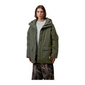 Modelo con la parka acolchada Carhartt WIP Stanwood Parka en color Cypress abierta, en plano medio, con capucha, bolsillos de parche y etiqueta cuadrada en el bajo.