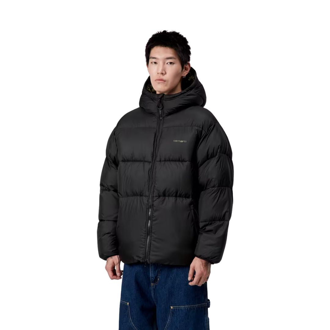 Modelo masculino vistiendo chaqueta Carhartt WIP Toronto Jacket color Black Camo Duck Green vista trasera mostrando capucha y acolchado.