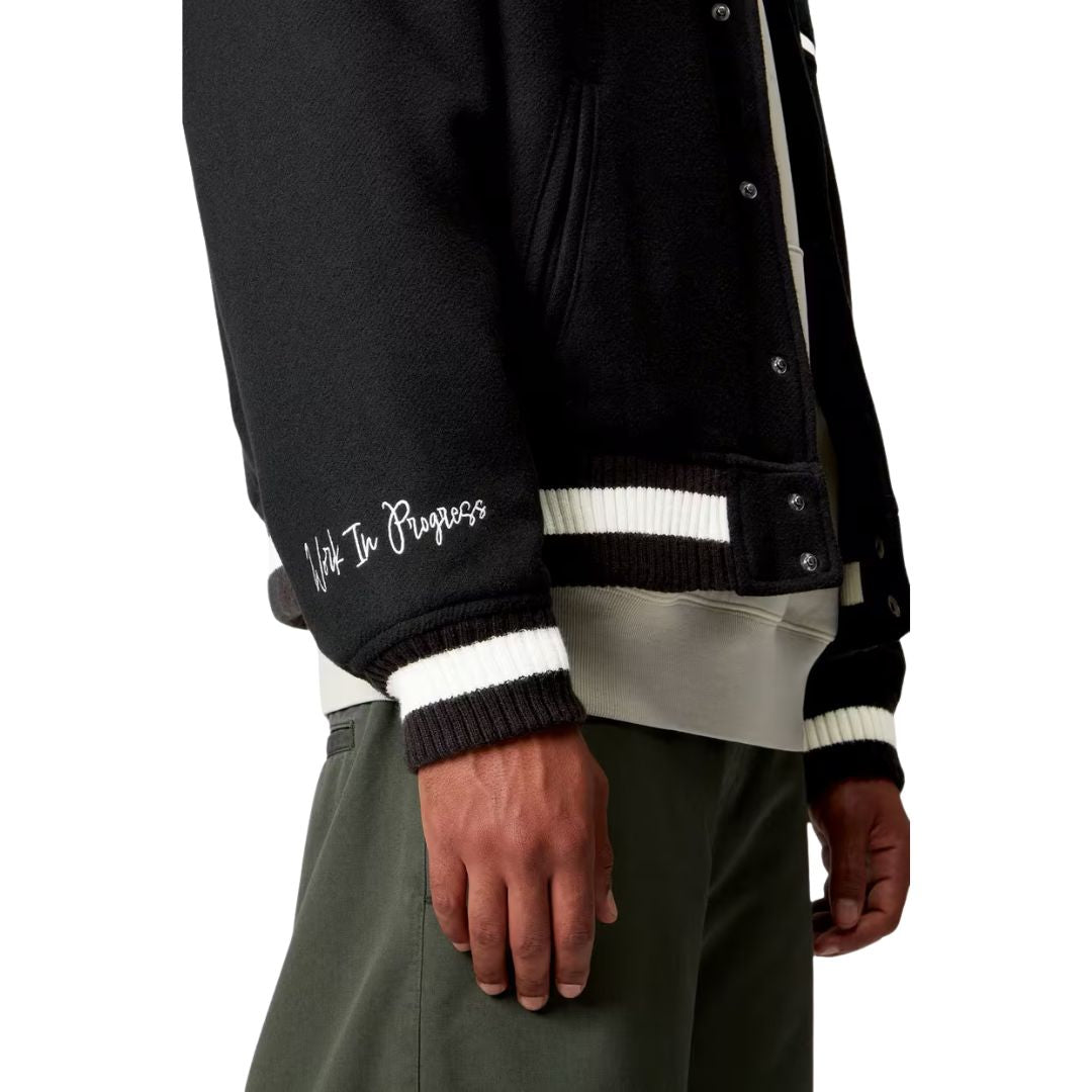 Detalle lateral de la chaqueta Carhartt WIP World Class Varsity color Black mostrando puño y bordado Work In Progress.